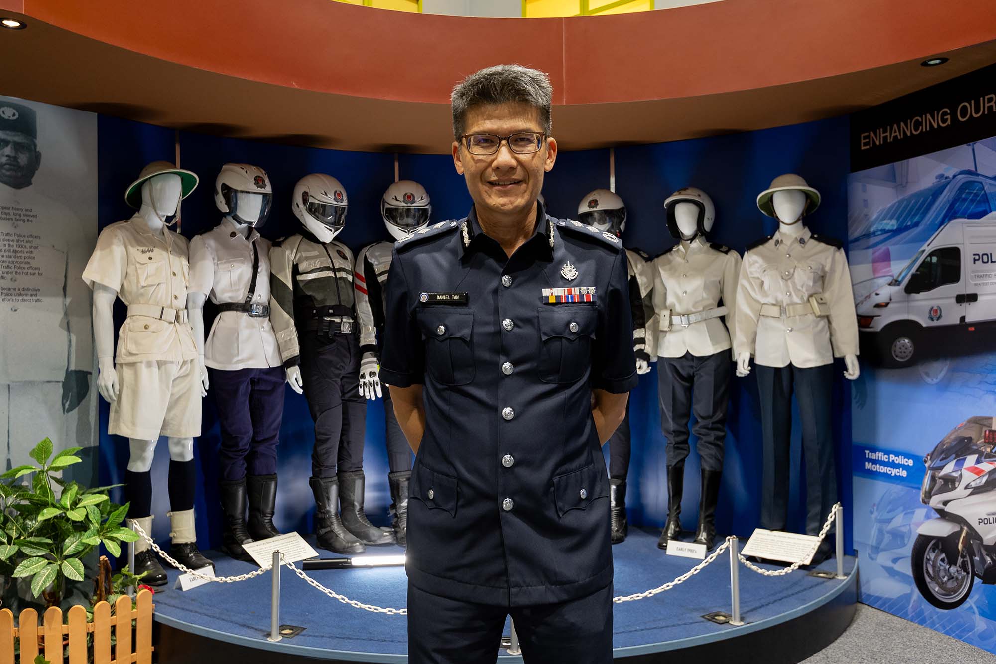 SAC Daniel Tan in uniform, standing infront of an exhibit that shows different TP uniforms over the years