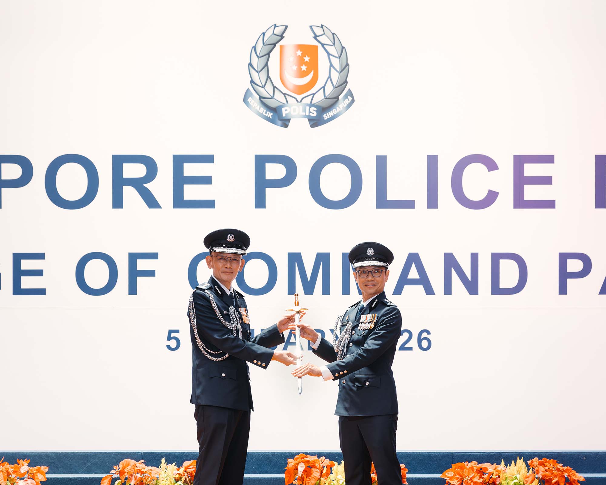 photo of Mr hoong wee teck passing the sword over to Mr How Kwang Hwee. Both are wearing a ceremonial dark blue uniform and standing infront of a big backdrop stating Singapore Police Force Change of Command Parade