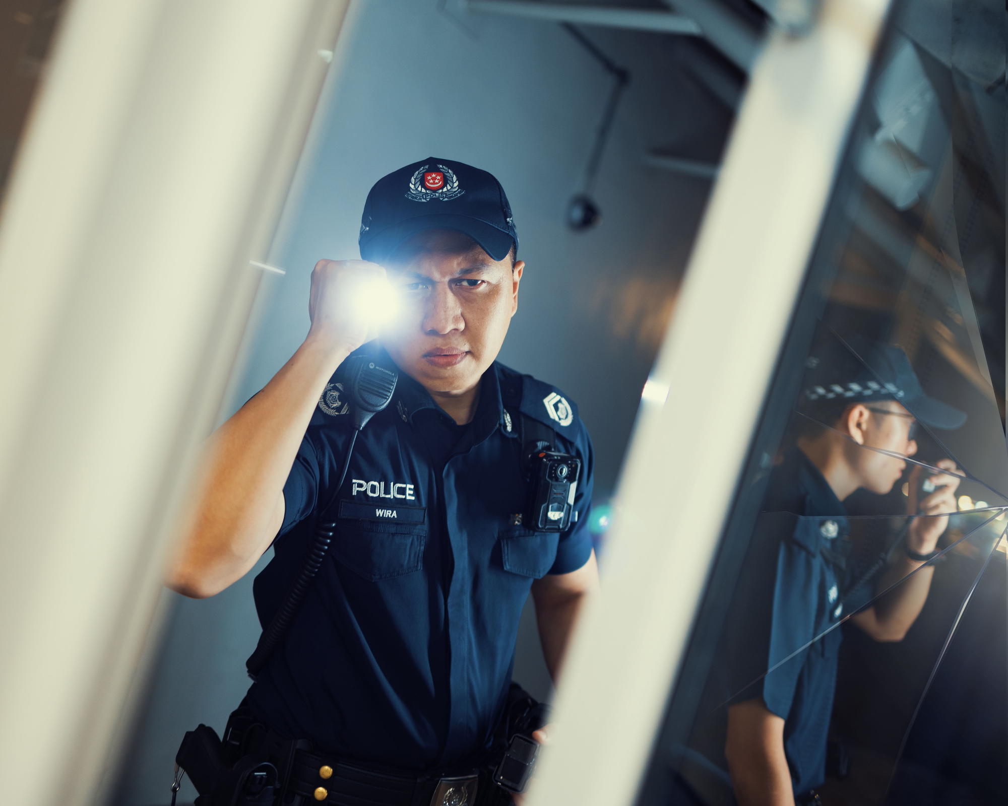 a police officer shining a torchlight towards a glass pane that is reflecting. It is shown to be cracked. 