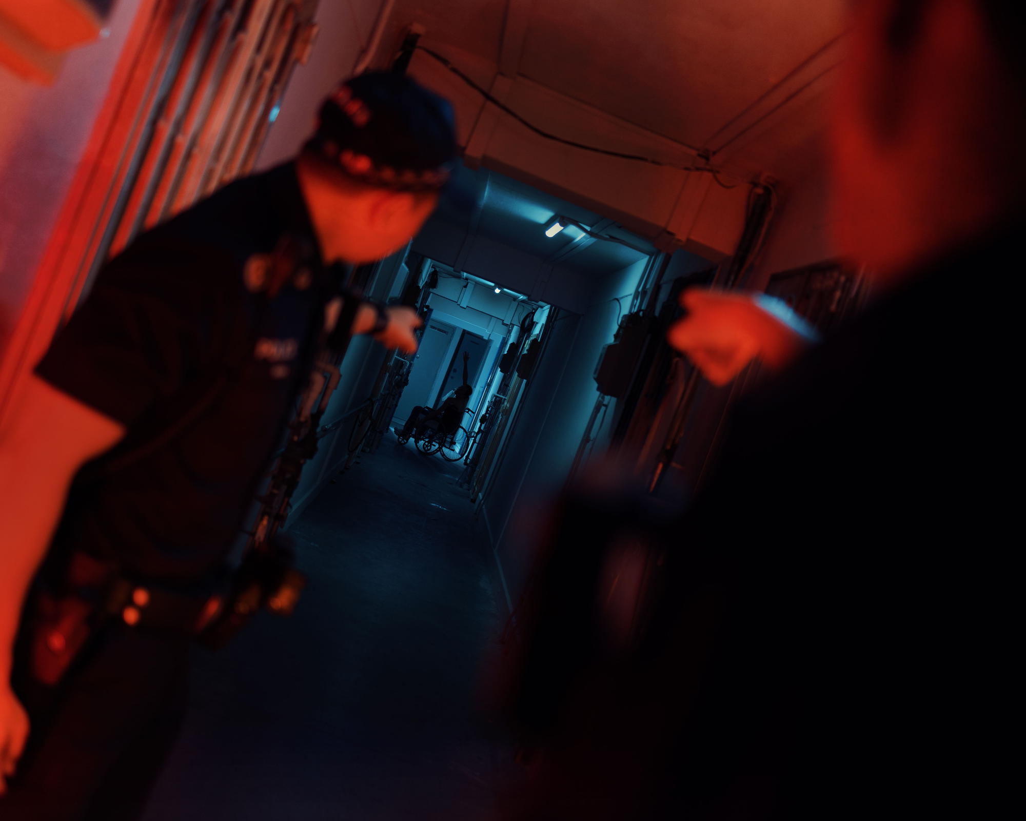 two officers in a alleyway of a dark hdb unit, pointing towards the end of alleyway where a silhouette of an old man in a wheelchair can be seen.