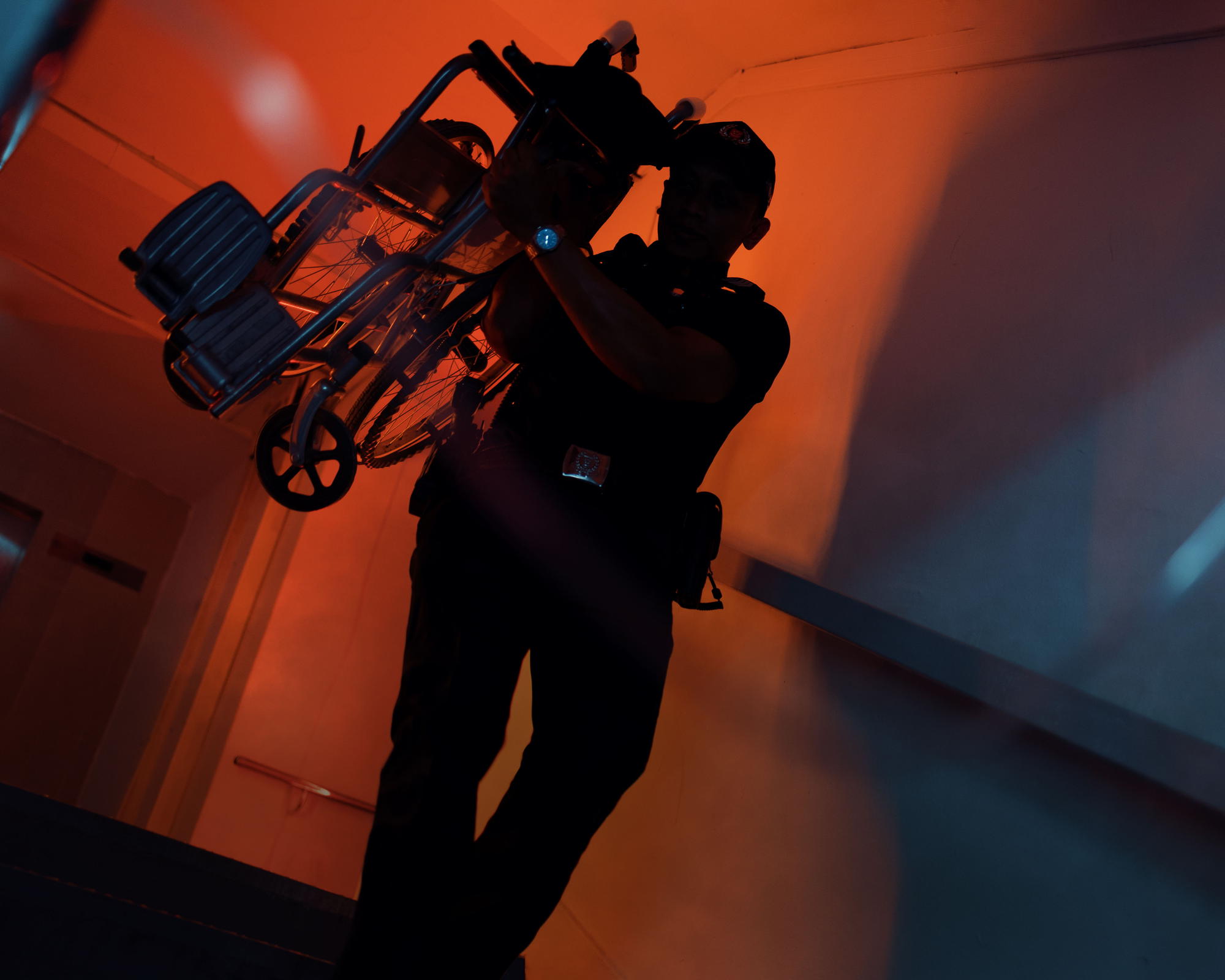 a silhouette with orange light seen in the background of an officer's silhouette. He is carrying a wheelchair using right arm.