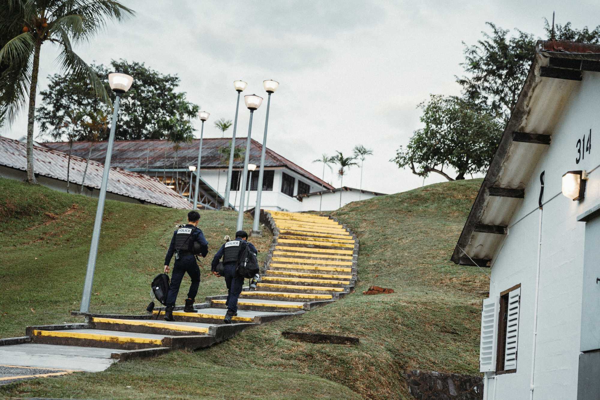 two officer seen climbing a hill on a narrow staircase in an outdoor setting. They are proceeding to a building on top of the hill