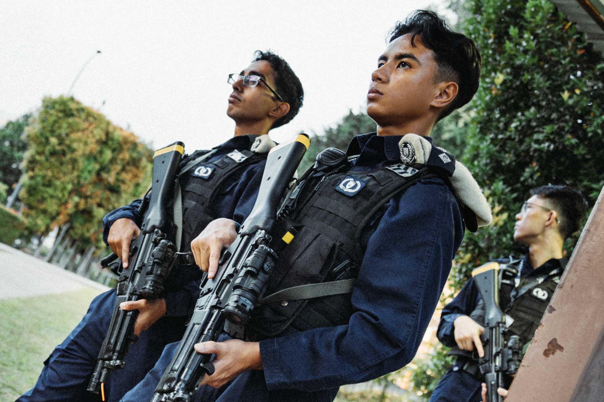 two officers in police uniform holding their firearms and standing in attention, facing the 9pm direction. There's another officer in the background looking around too