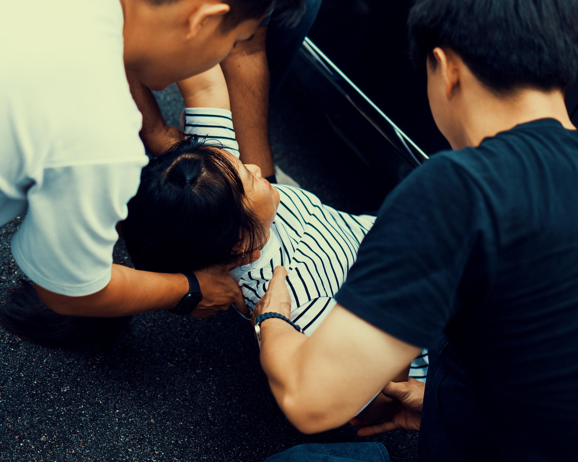 three men are around a lady in striped white top and the officer is securing her neck and people are pulling her out