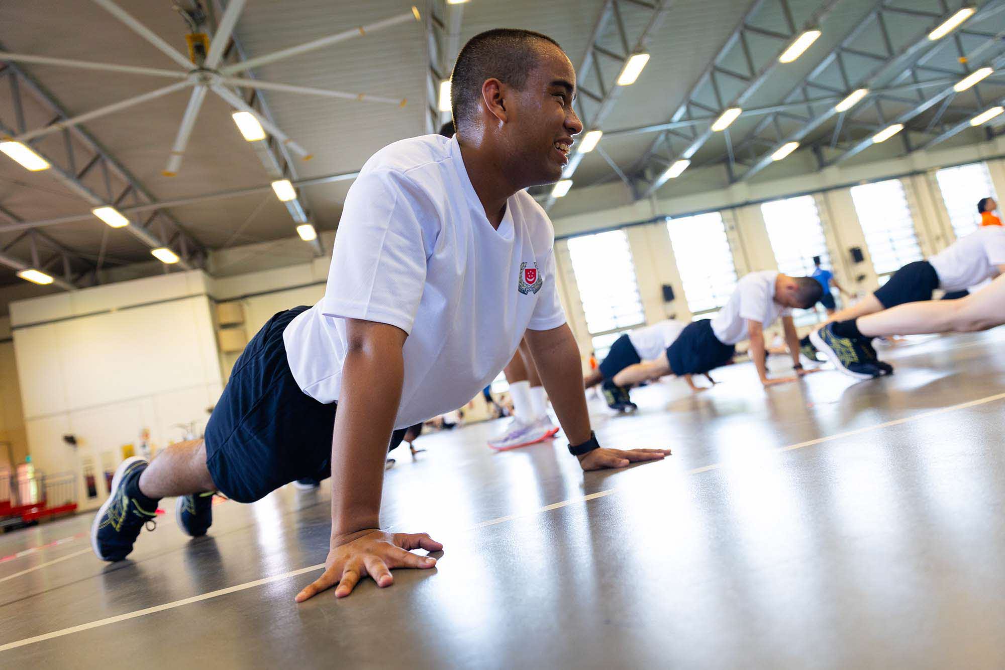 Doing push-ups and jumping jacks together as a squad in the multi-purpose hall.