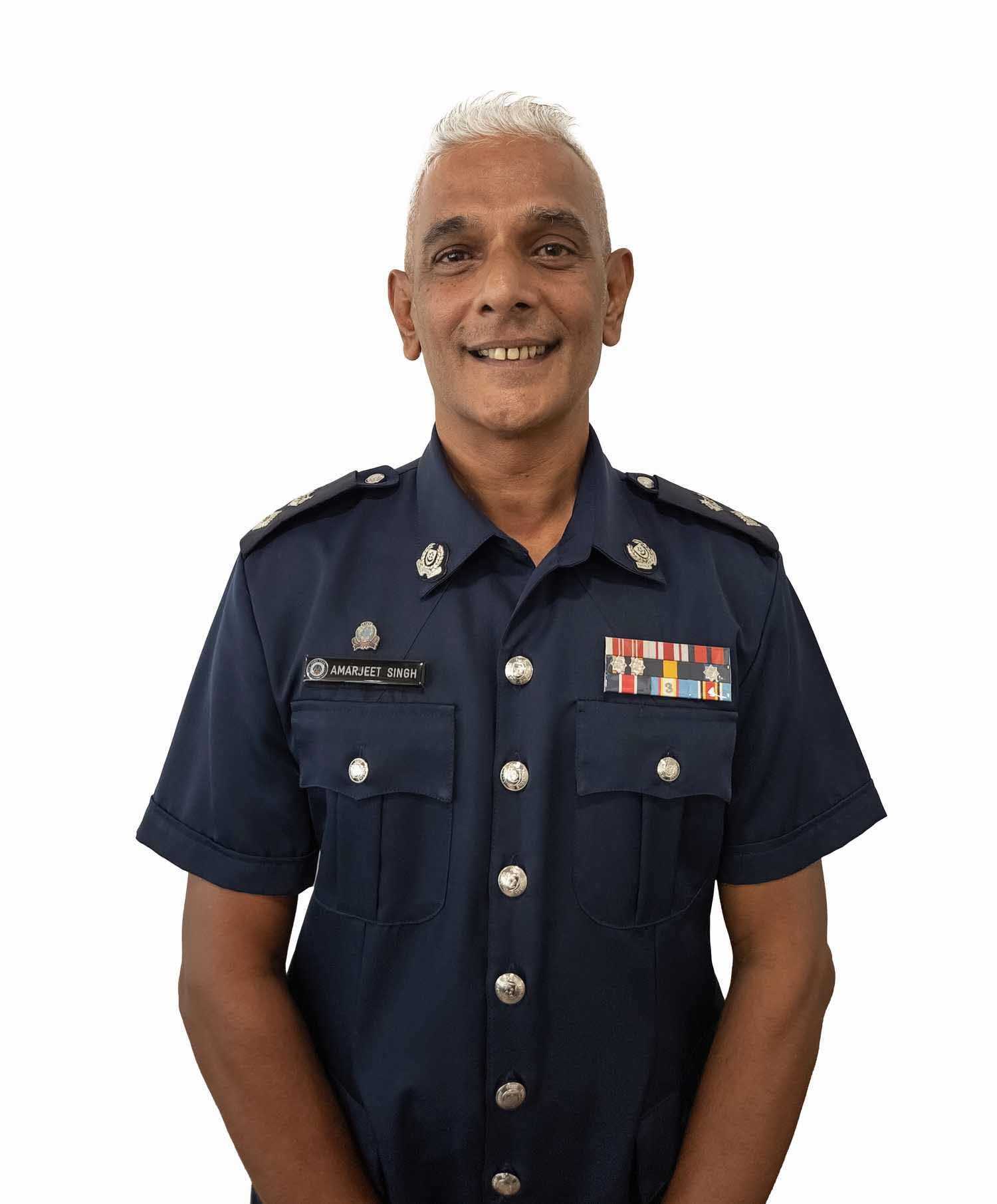 a profile shot of DSP Amarjeet Singh in uniform, with many medals and ribbons, standing infront of a white background. 