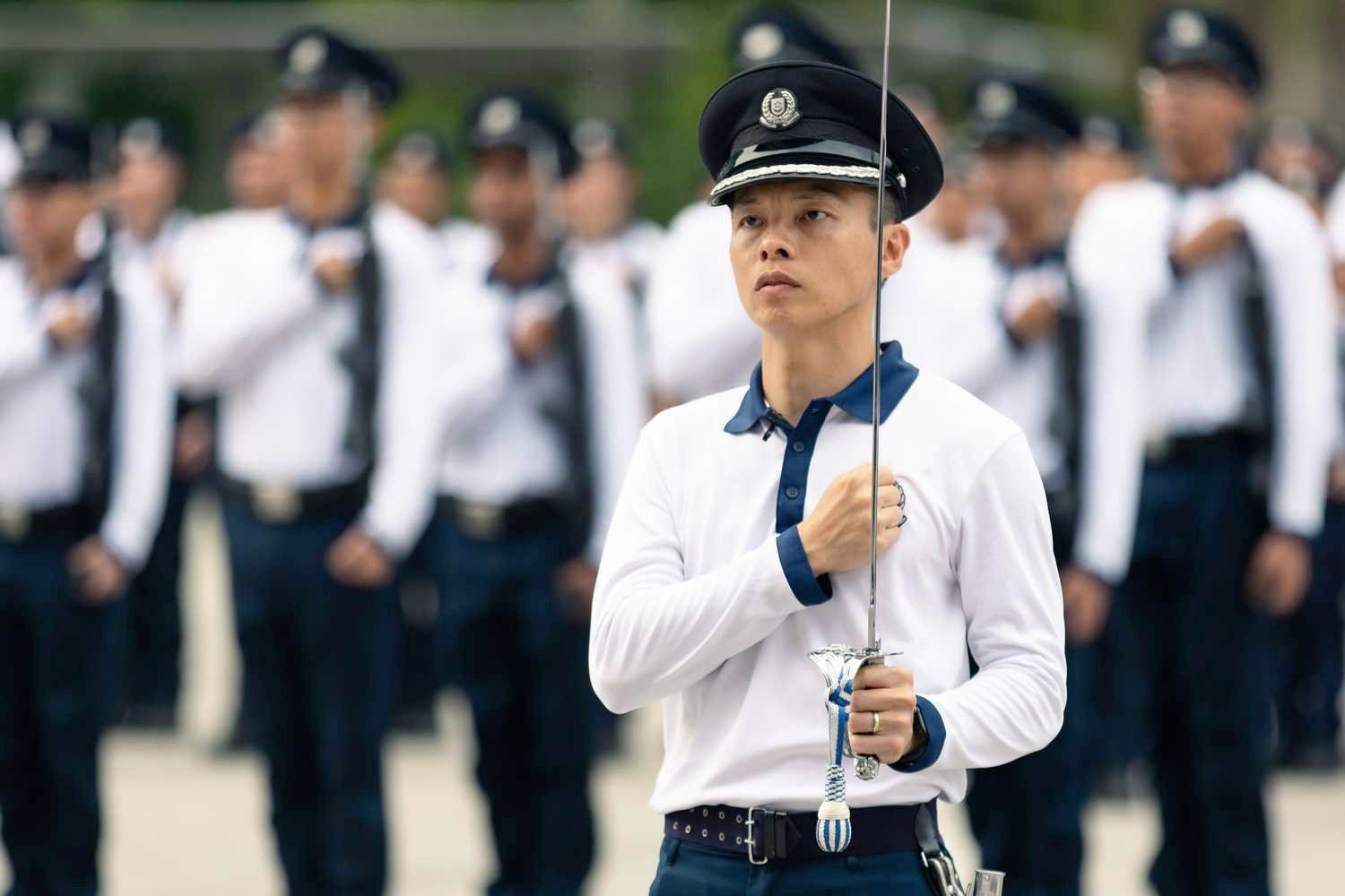 photo of DAC Tan wearing a white long sleeve rehearsal attire, holding a sword and taking the police pledge, with his fist clenched on his left chest