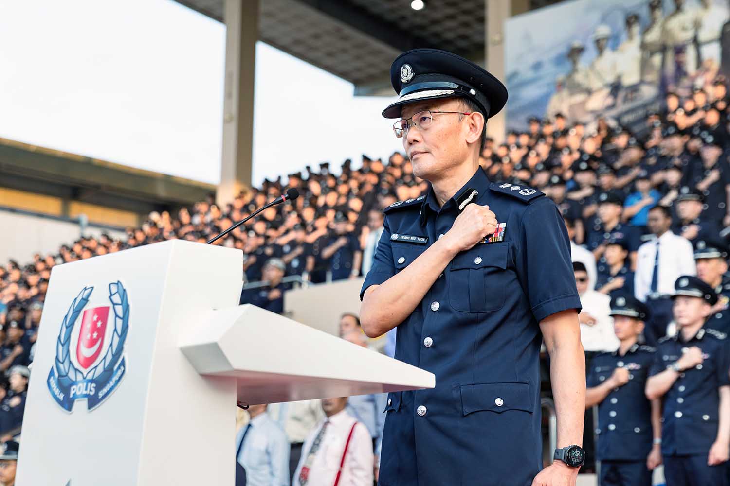 photo of Commissioner of Police taking the pledge at the rostrum, with the spectators at the back of him