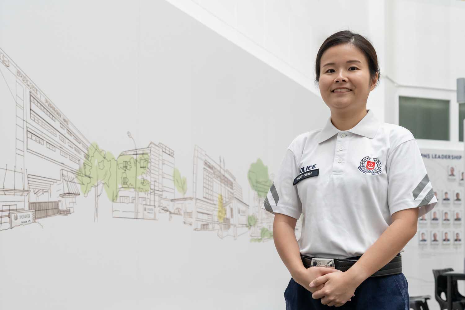 sergeant sally in her white cpu polo tee, standing infront of a wall with a mural. The mural design is architectural like and vectored