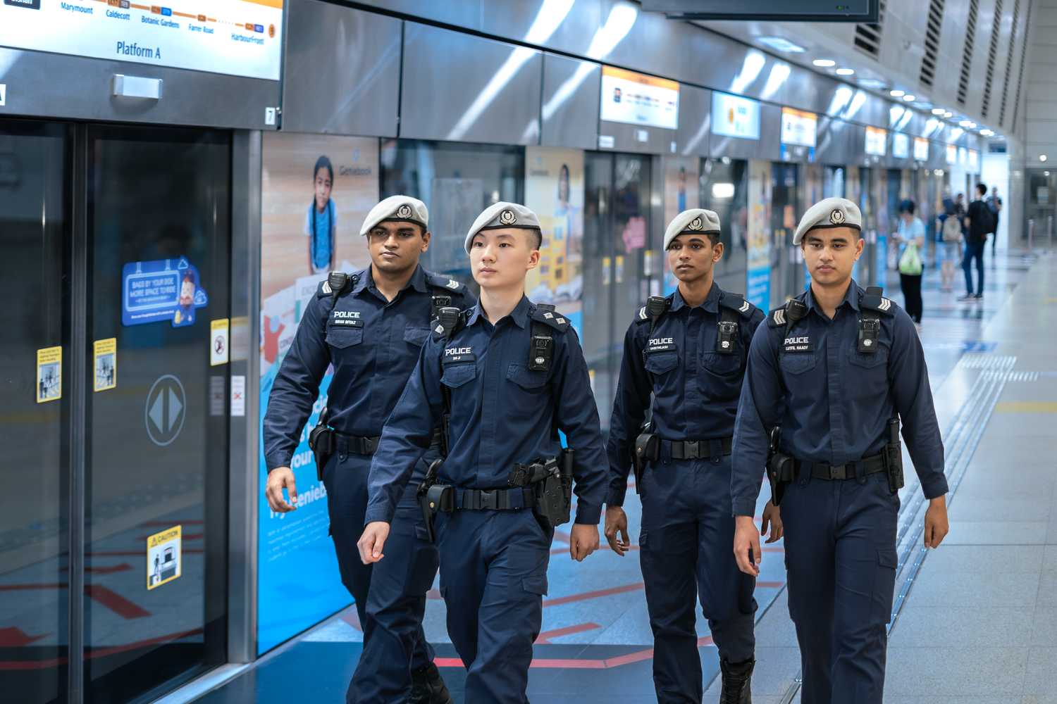 four officers in blue uniform , grey beret and full gear patrolling the platform of an underground MRT