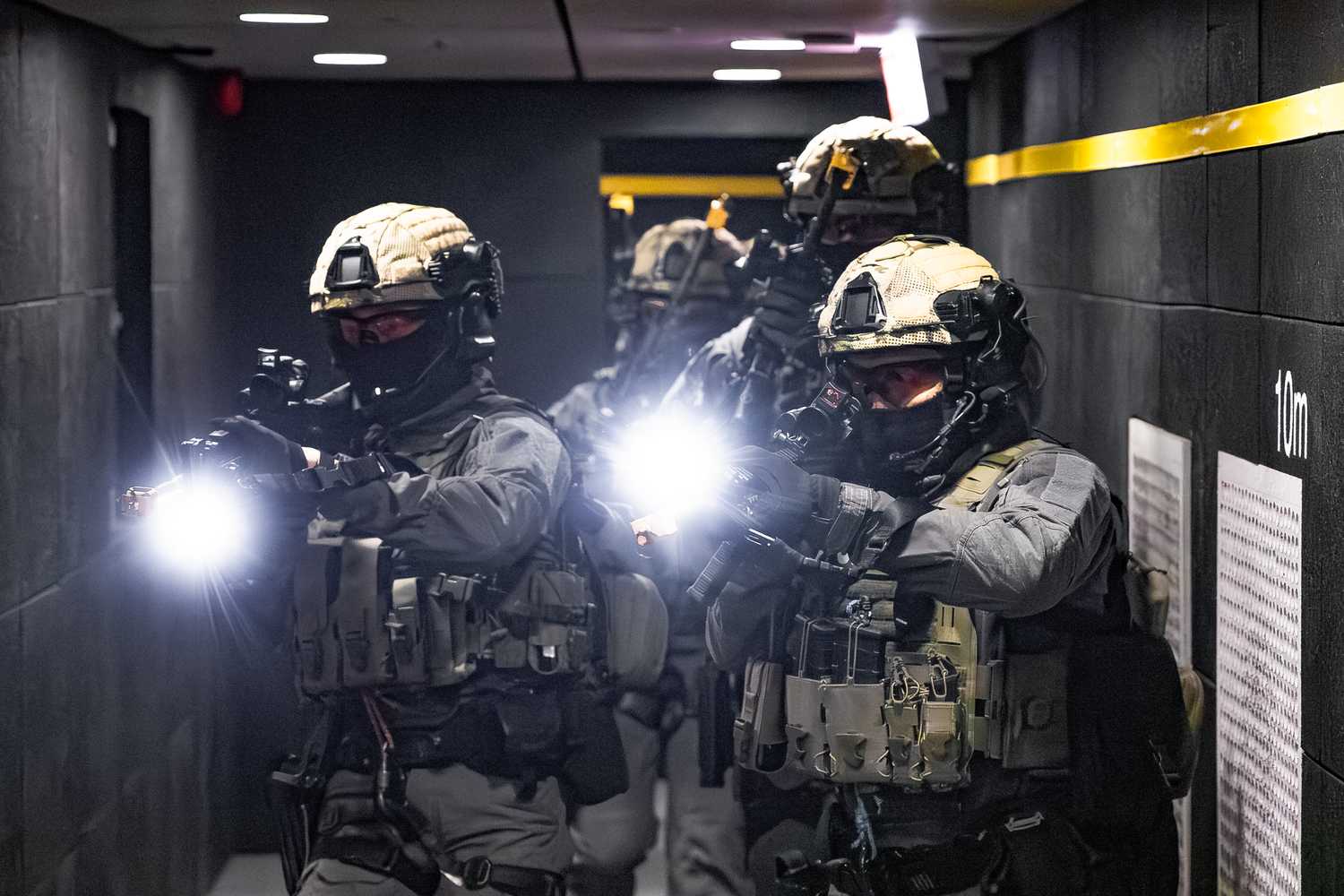 heavily armed SPF officers in light green gear storming a narrow pathway with their guns. There is a light shining from their muzzle