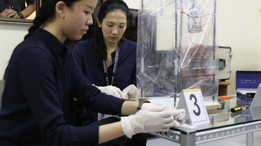 A gif of two Forensic Specialists at a table setting up the Portable Fingerprint Development Chamber.