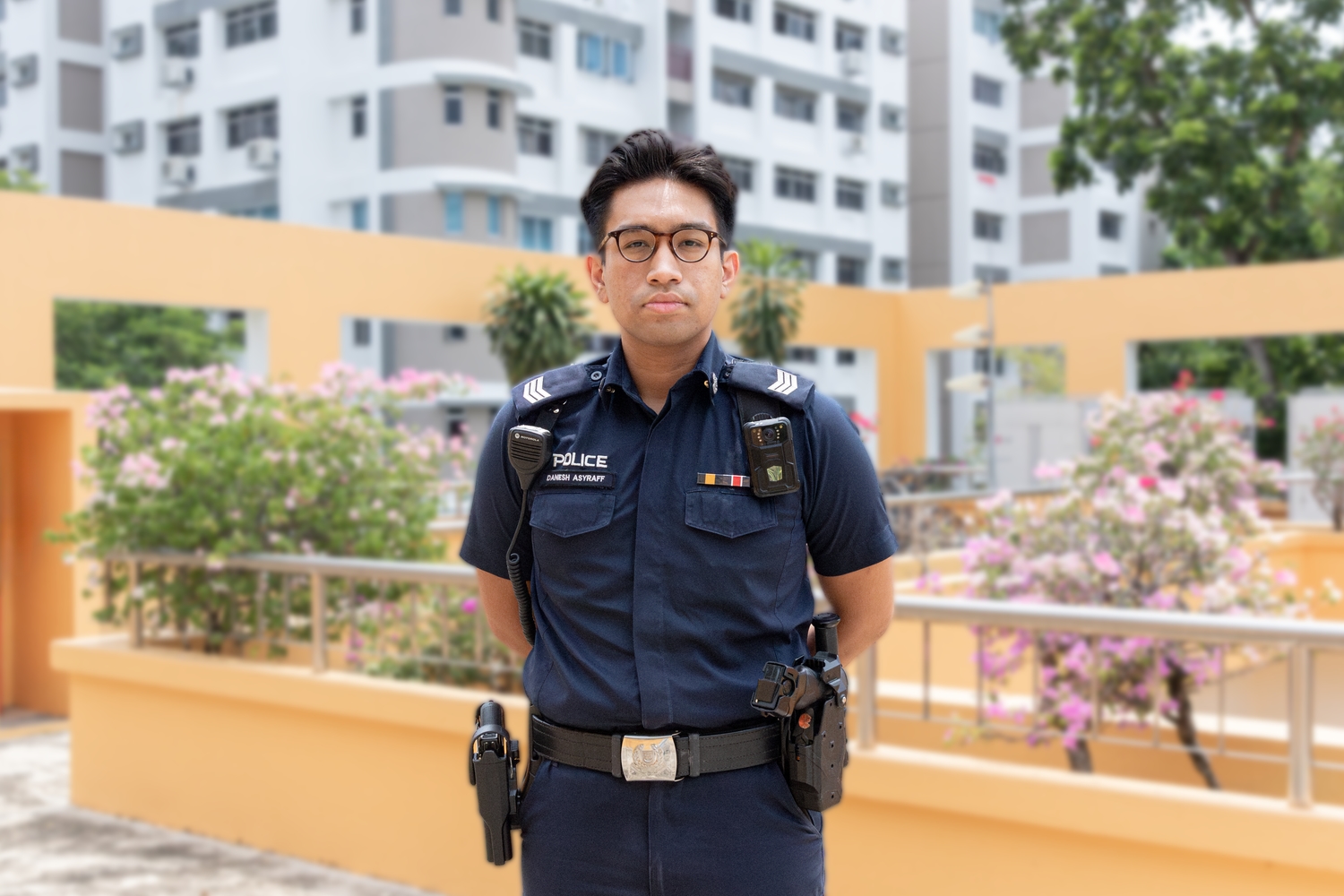 police officer standing with his arms to the back, against a yellow and beige building which is the rooftop of the NPC