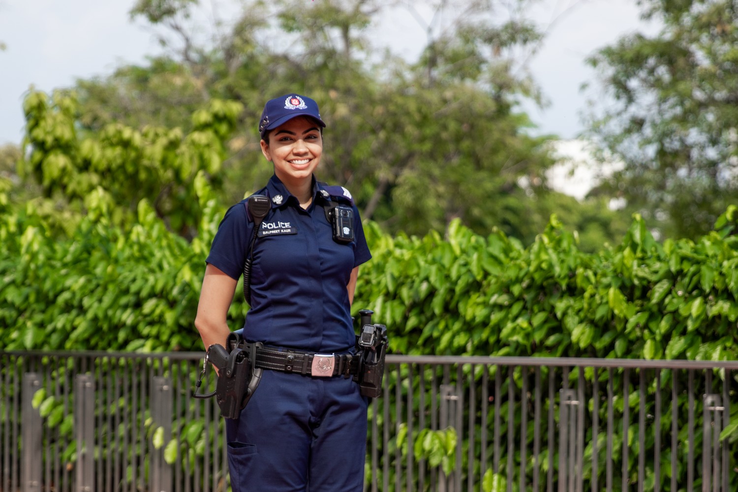 female officer in uniform standing and posing for camera. Behind her is a railing with the canopy of trees sticking out