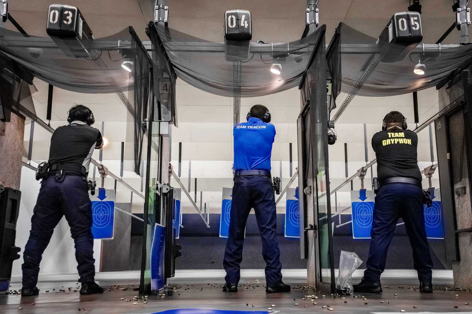 officers in position standing and shooting their guns in the range. Photo is taken from the back of three officers in the aisles