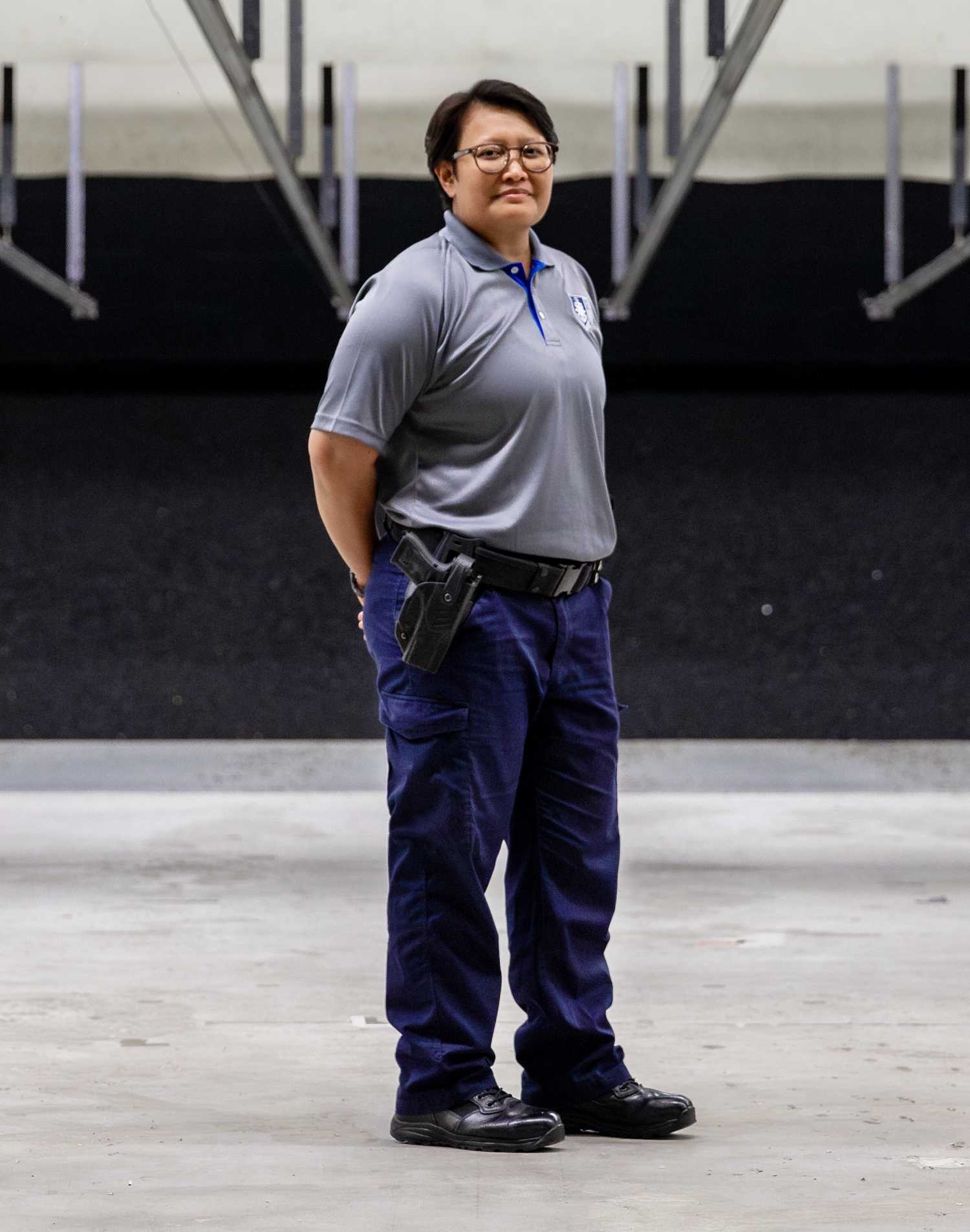 female officer standing in the range, wearing a grey polo tee, smiling for photo