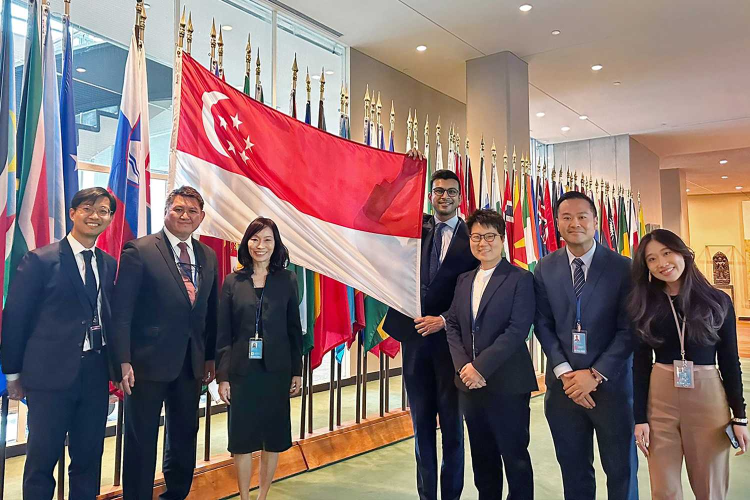 group of officers wearing formal attire, with blazer, carrying a singapore flag in the middle