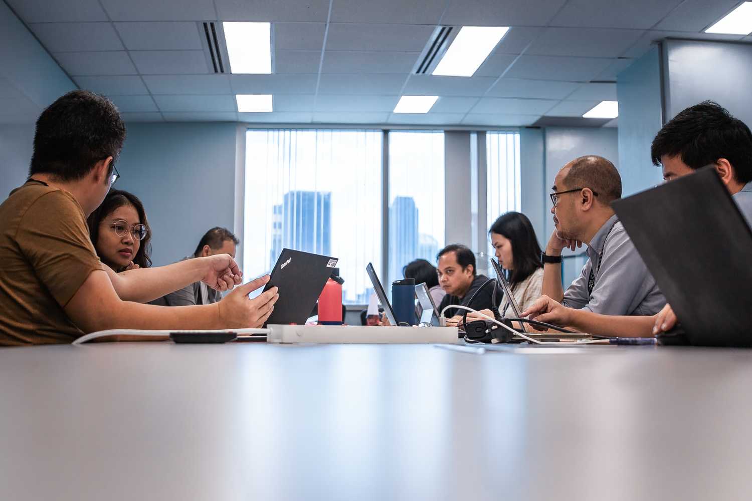 A low-angle shot of people sitting at a table with their laptops out and in the midst of a discussion. The scene is meant to depict a preproduction meeting, where the production team, Investigator Officers and other stakeholders discuss how to bring the case to life on-screen.