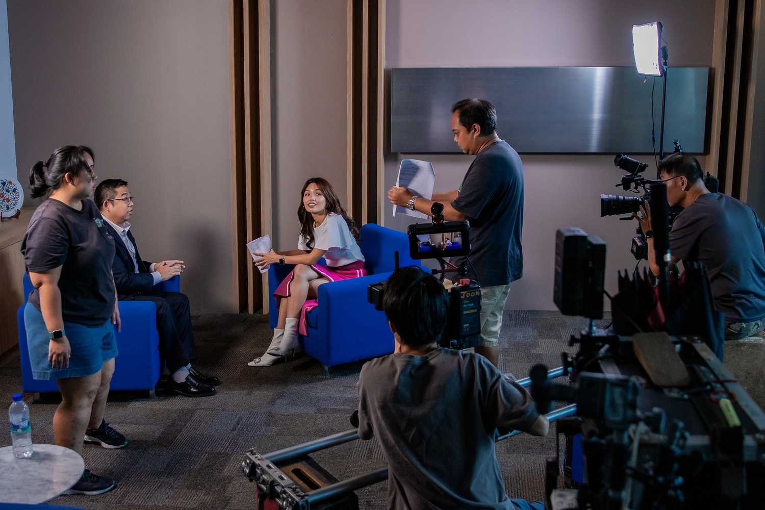 The picture depicts Mediacorp artiste Hazelle Teo interviewing NCPC Council Member Mr Nicholas Aaron Khoo for a 2023 Scam Alert segment. Behind them, the crew is filming.