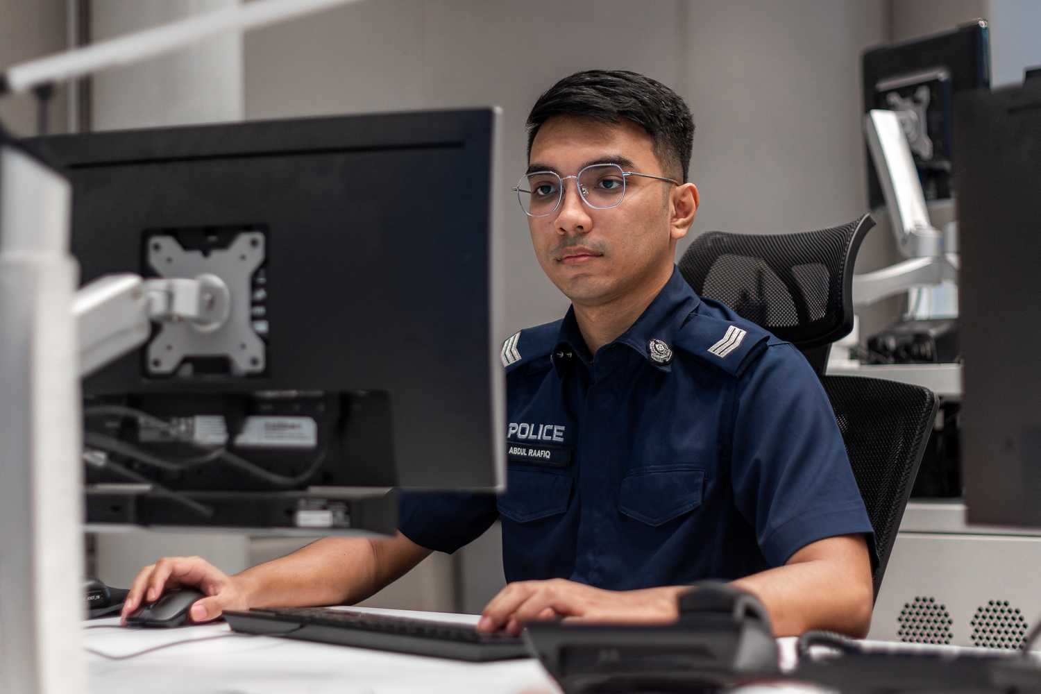 a full time police national service officer sitting inside POCC, facing a computer that is not visible to the viewer