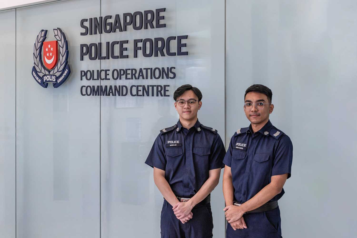 two pnsfs standing infront of a wall that reads Police Operations Command Centre, and posing with their hands locked infront of them, 