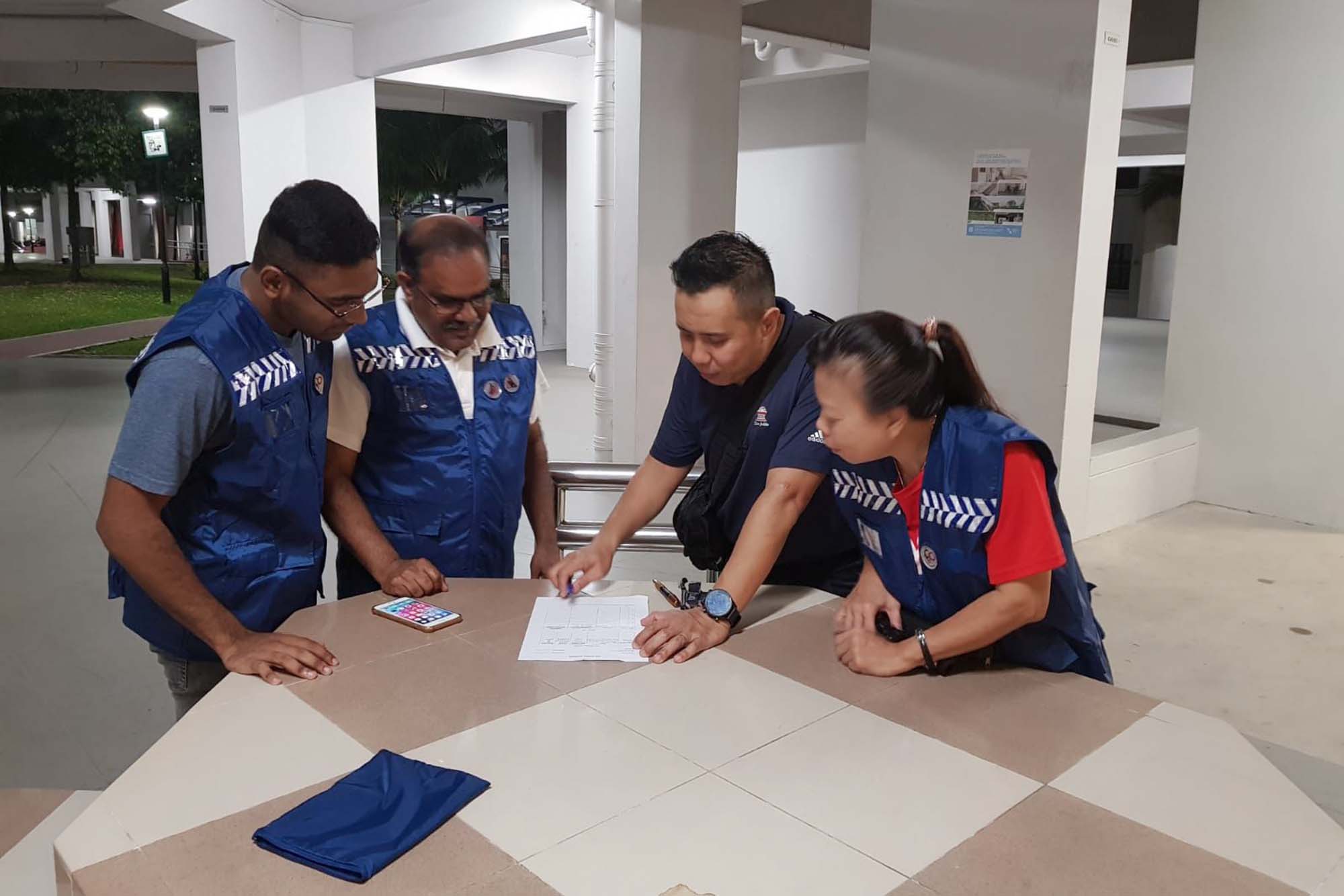 four civilians wearing blue vests discussing at a voiddeck, looking at a piece of paper placed on the voiddeck table