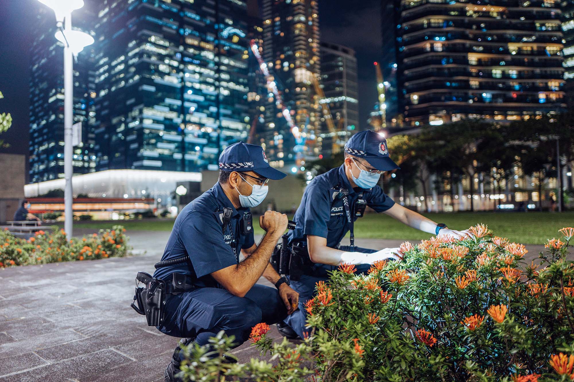two officers squatting and shining their torchlight into the bushes