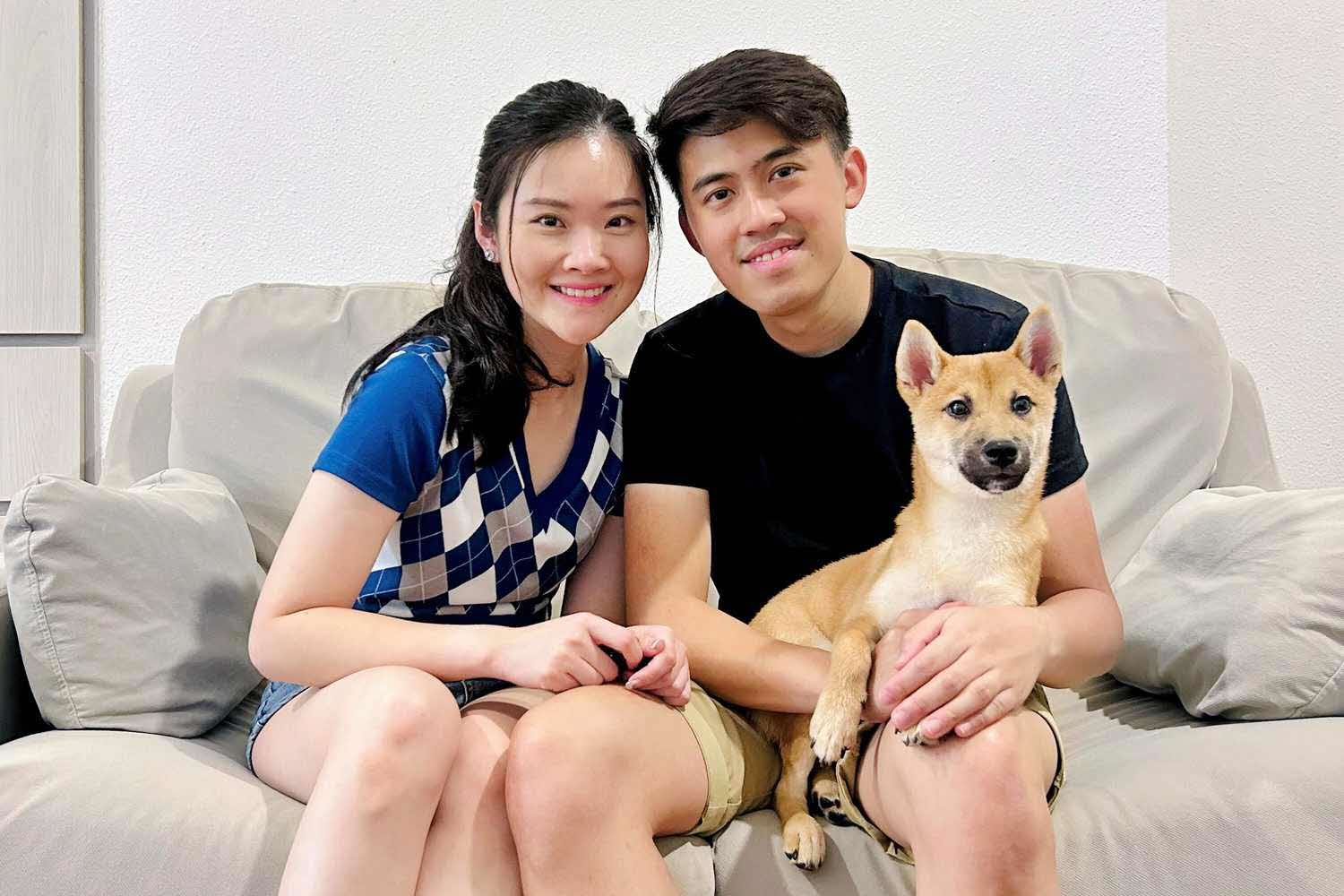 a couple sitting on a sofa with a shiba inu dog