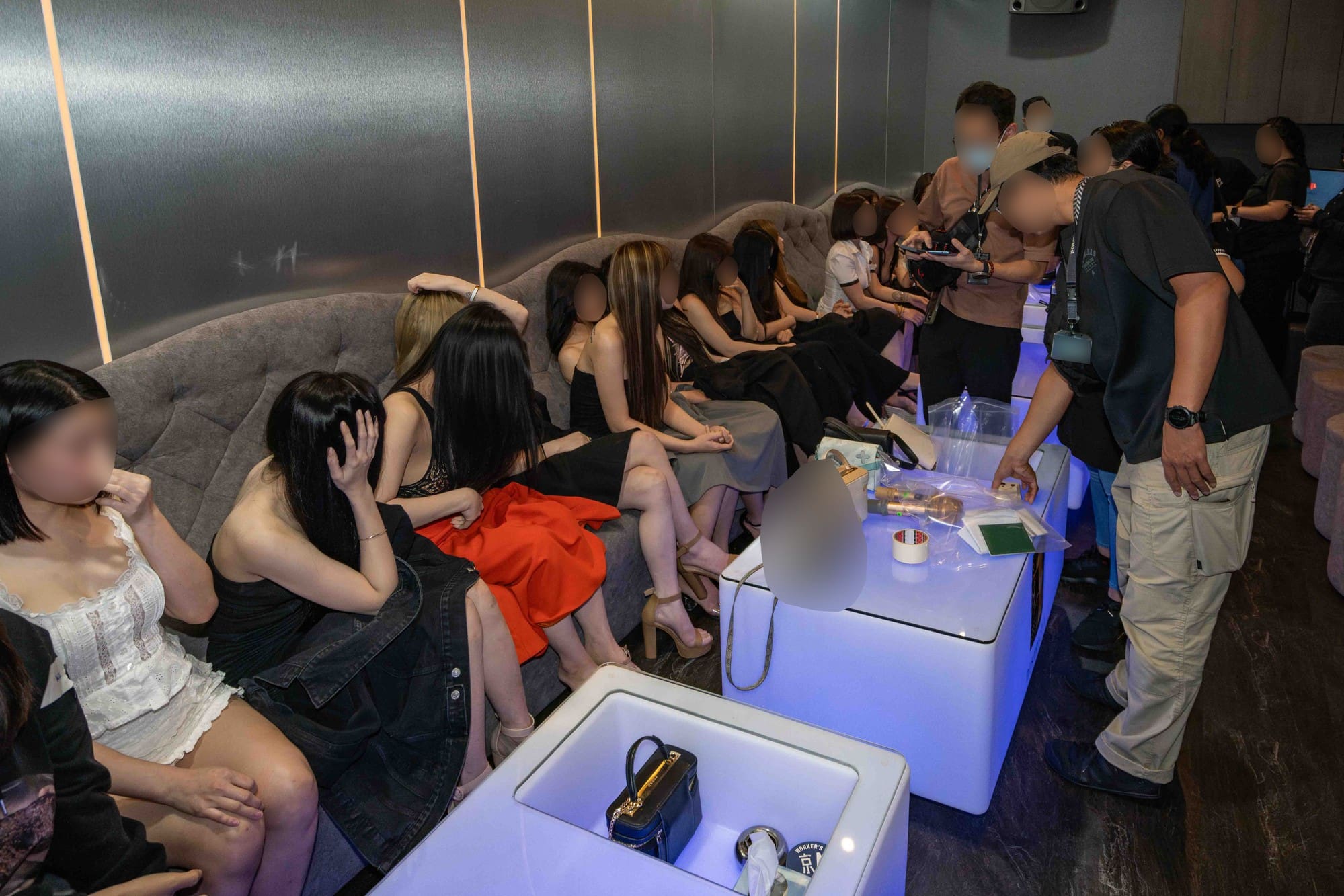 a photo of a ktv lounge with many women seated on a long sofa chair being checked by police officers
