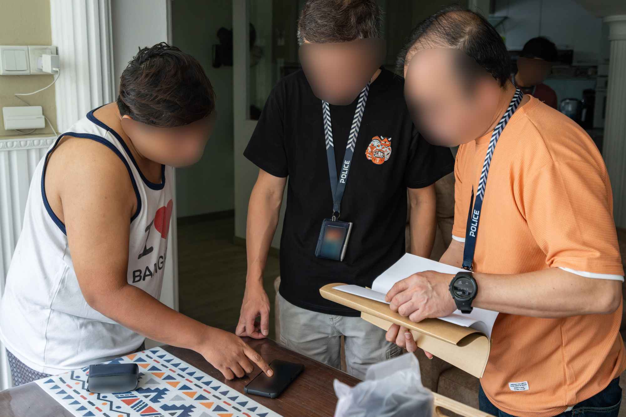 two officers in black and orange casual wear, respectively, asking a male subject in white singlet some questions