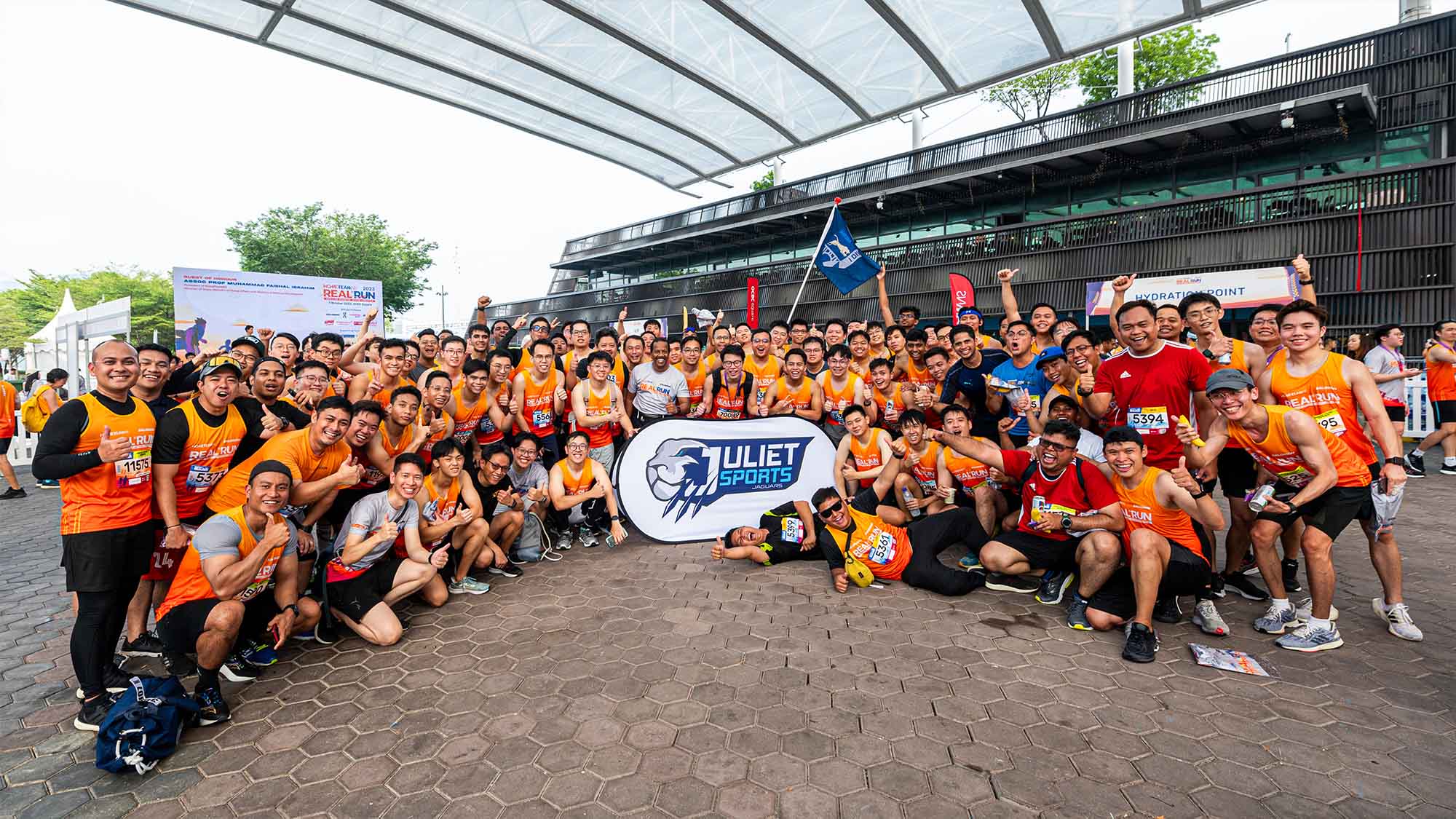 a large of officers in orange tees, part of the realrun, gathered together and posing for the photo. more than 50 people are seen in the photo