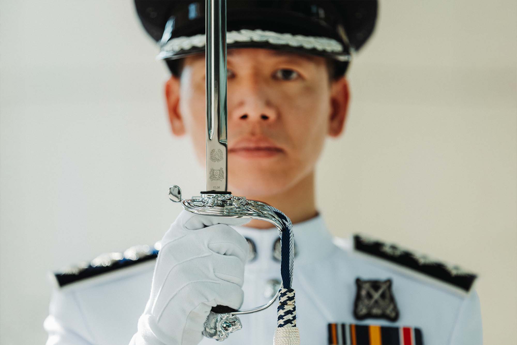 commander seen holding to sword to his face, with the details of the sword visible. it shows two police crests that are engraved on it