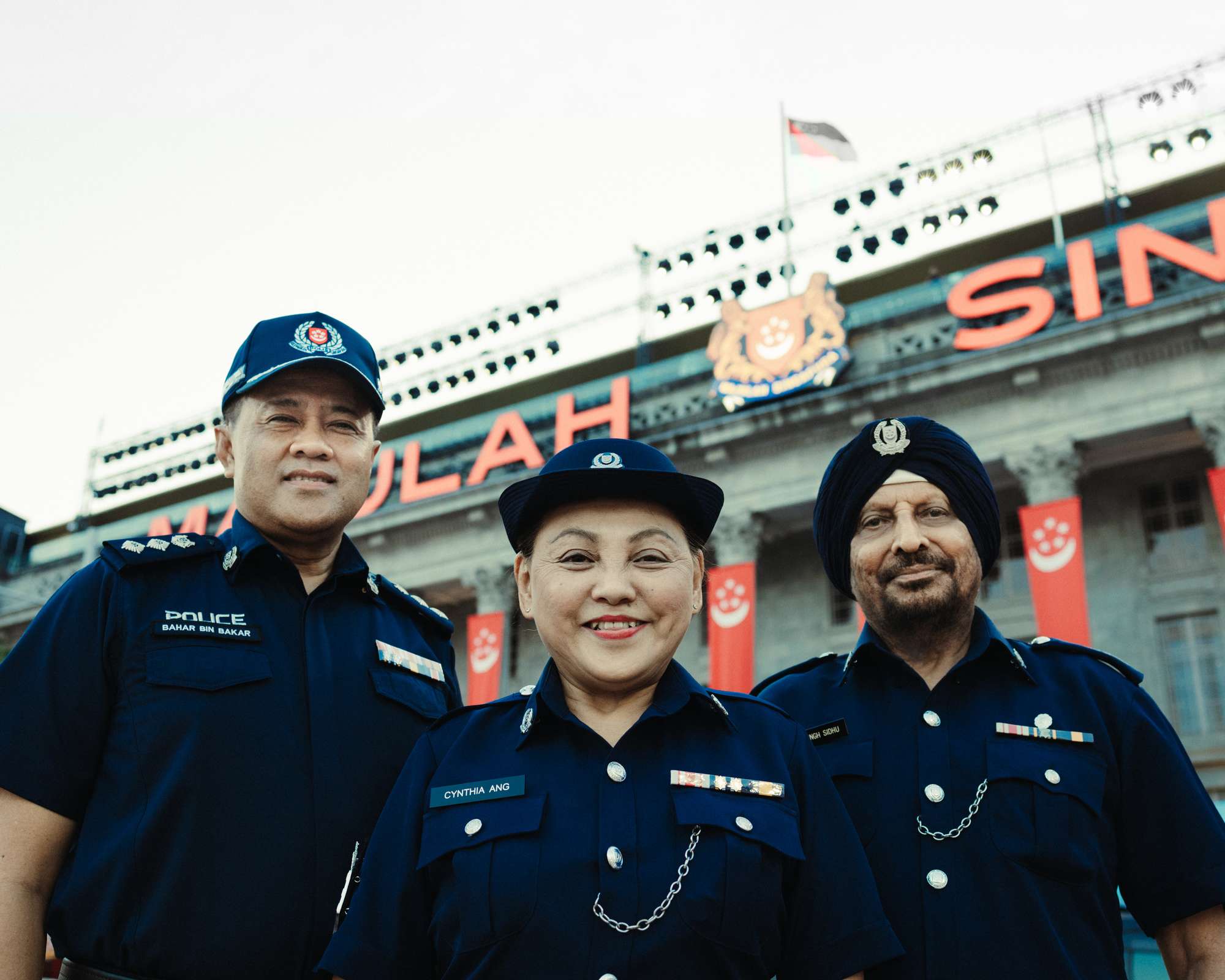three officers in uniform looking down at the camera together infront of the national gallery of singapore