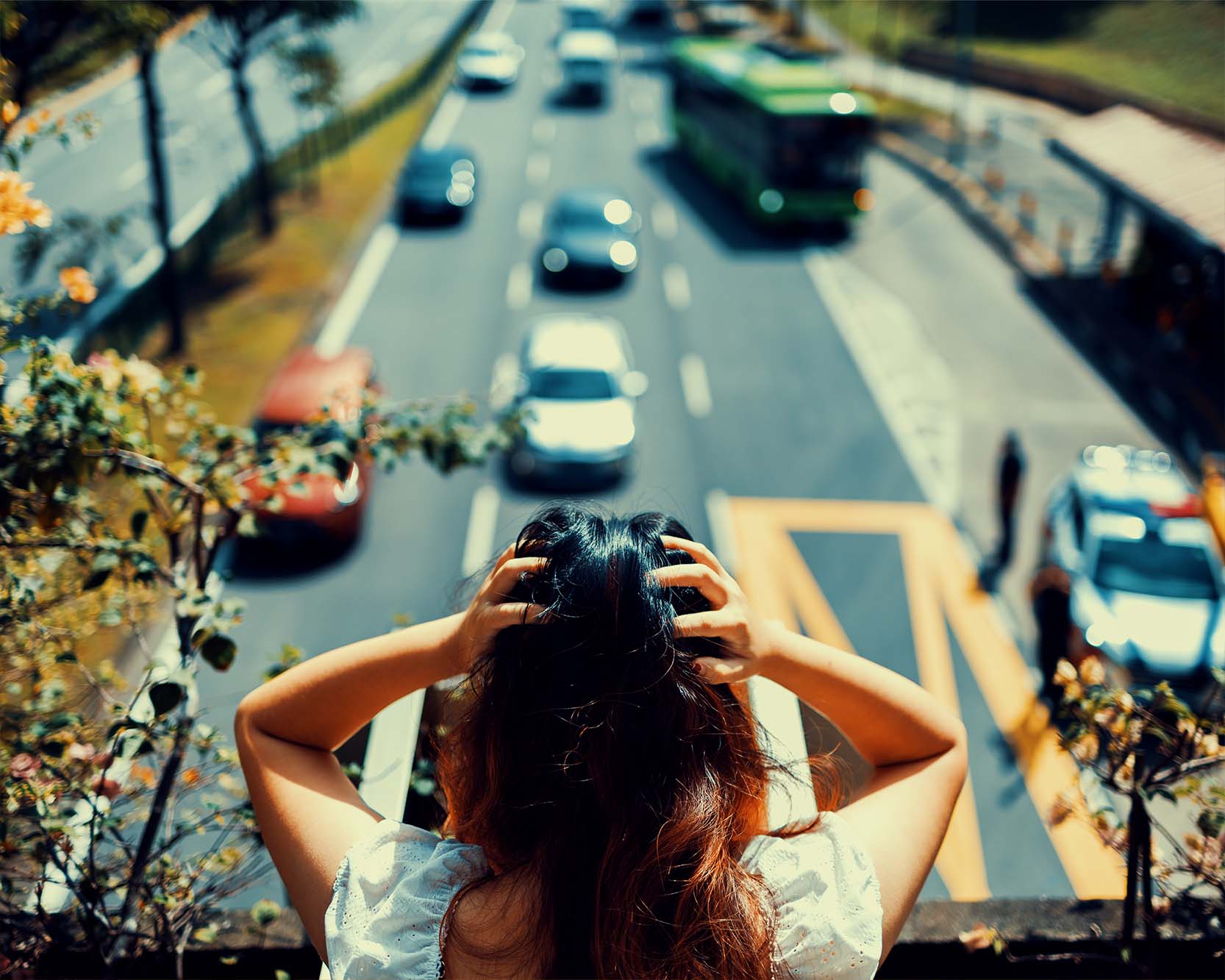 a woman wearing a white coloured top with red hair, seen squatting outside on the ledge of the overhead bridge