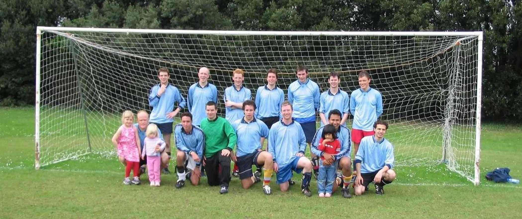 a football team photo of players wearing light blue jerseys and posing in a team photo setting on a field infront of a goalpost