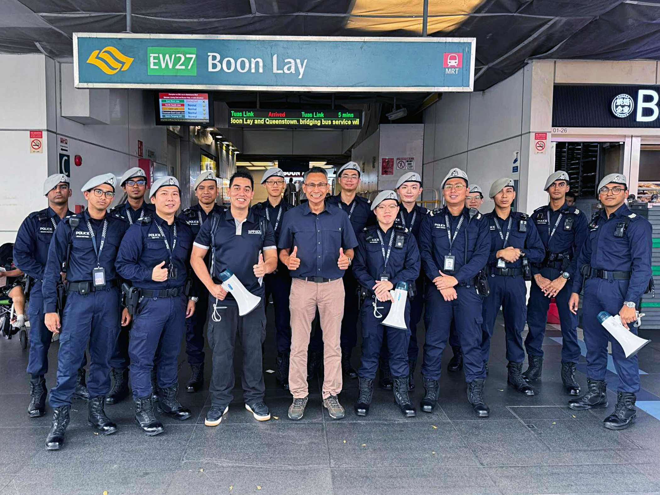 a group photo of transcom officers with commander in the middle and in civilian attire. They are standing infront of Boon Lay MRT