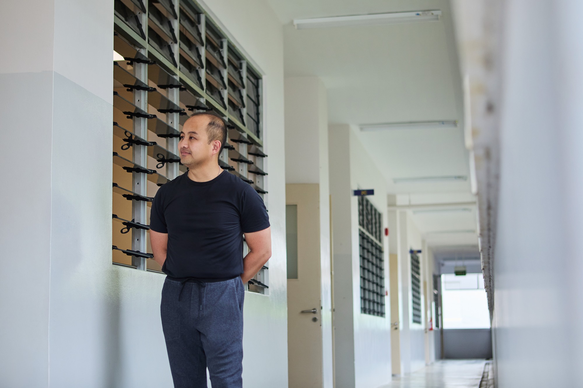 ASP Marc wearing a dark coloured t-shirt, tucked into his jeans, and walking by a classroom looking through the window. It is a leading line shot
